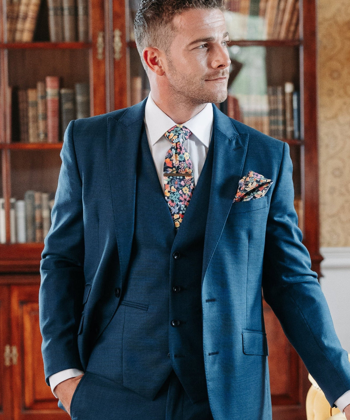 Man in a blue suit standing in a room with wooden floors and furniture.
