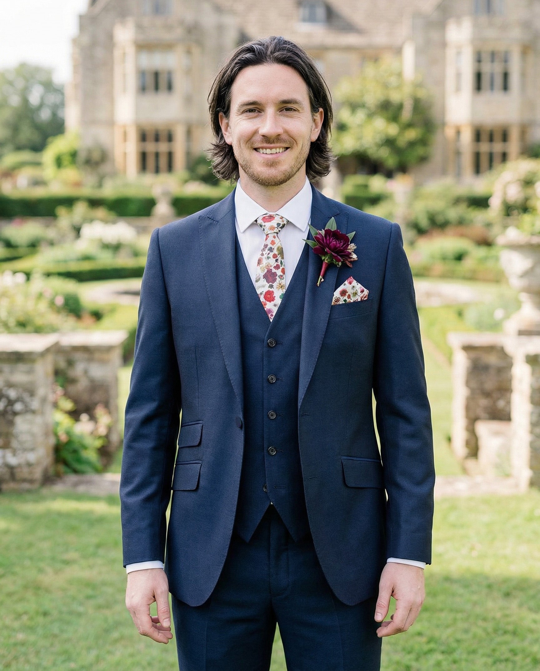 Groom wearing a navy mohair 3‑piece lounge suit for a wedding or formal event, crafted from lightweight, smooth fabric with a subtle sheen; includes tailored jacket, waistcoat, liberty of london tie and pocket square, a sharp menswear look available to hire or buy from Black Tie Menswear.